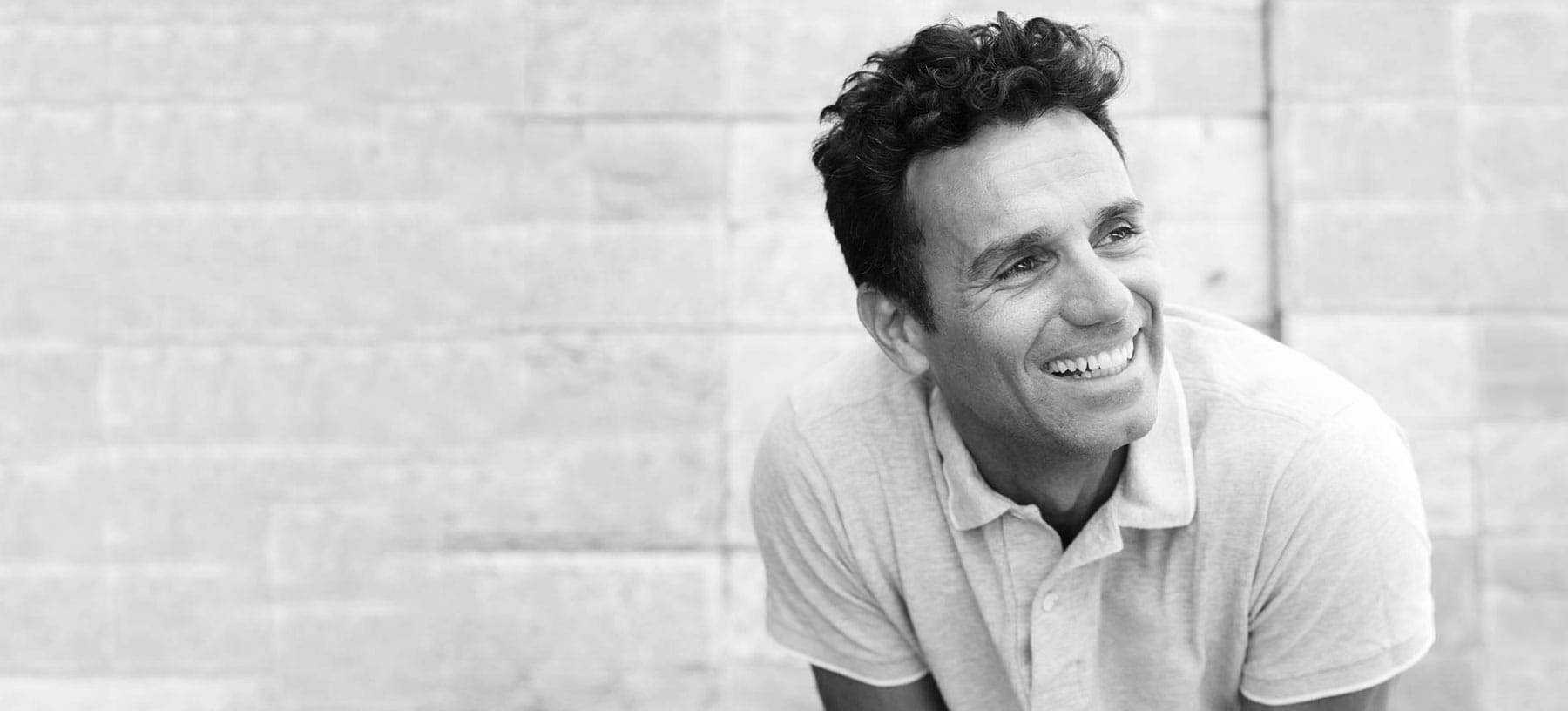 A relaxed man in a polo shirt smiling outdoors, representing the confidential mens health and erectile dysfunction care available at Optimal Well MD in Virginia Beach.