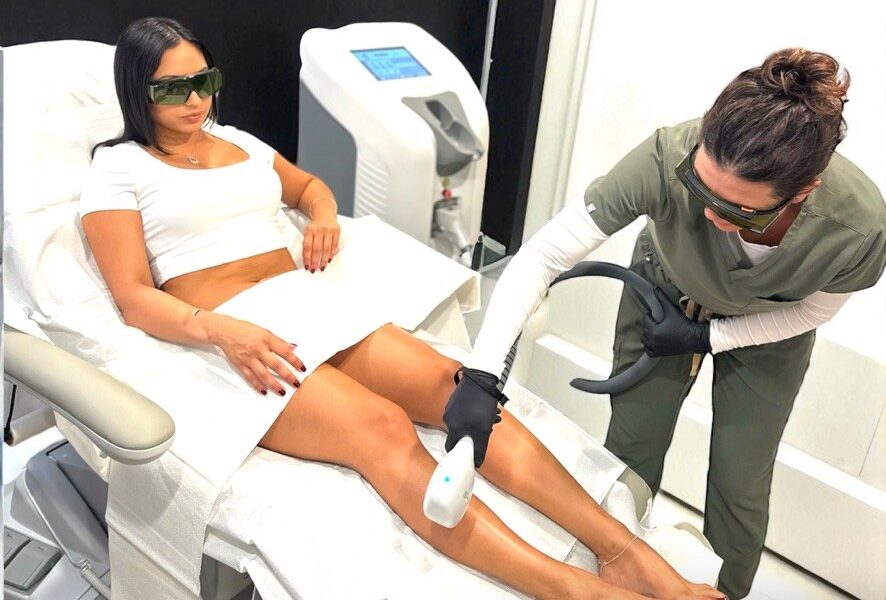 A provider in protective eyewear performs a laser hair removal treatment on a patient’s lower leg in a treatment room at Optimal Well MD in Virginia Beach