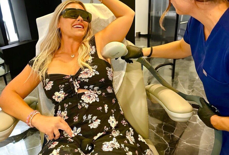 A patient wearing protective eyewear smiles during an underarm laser hair removal treatment performed by a provider at Optimal Well MD in Virginia Beach